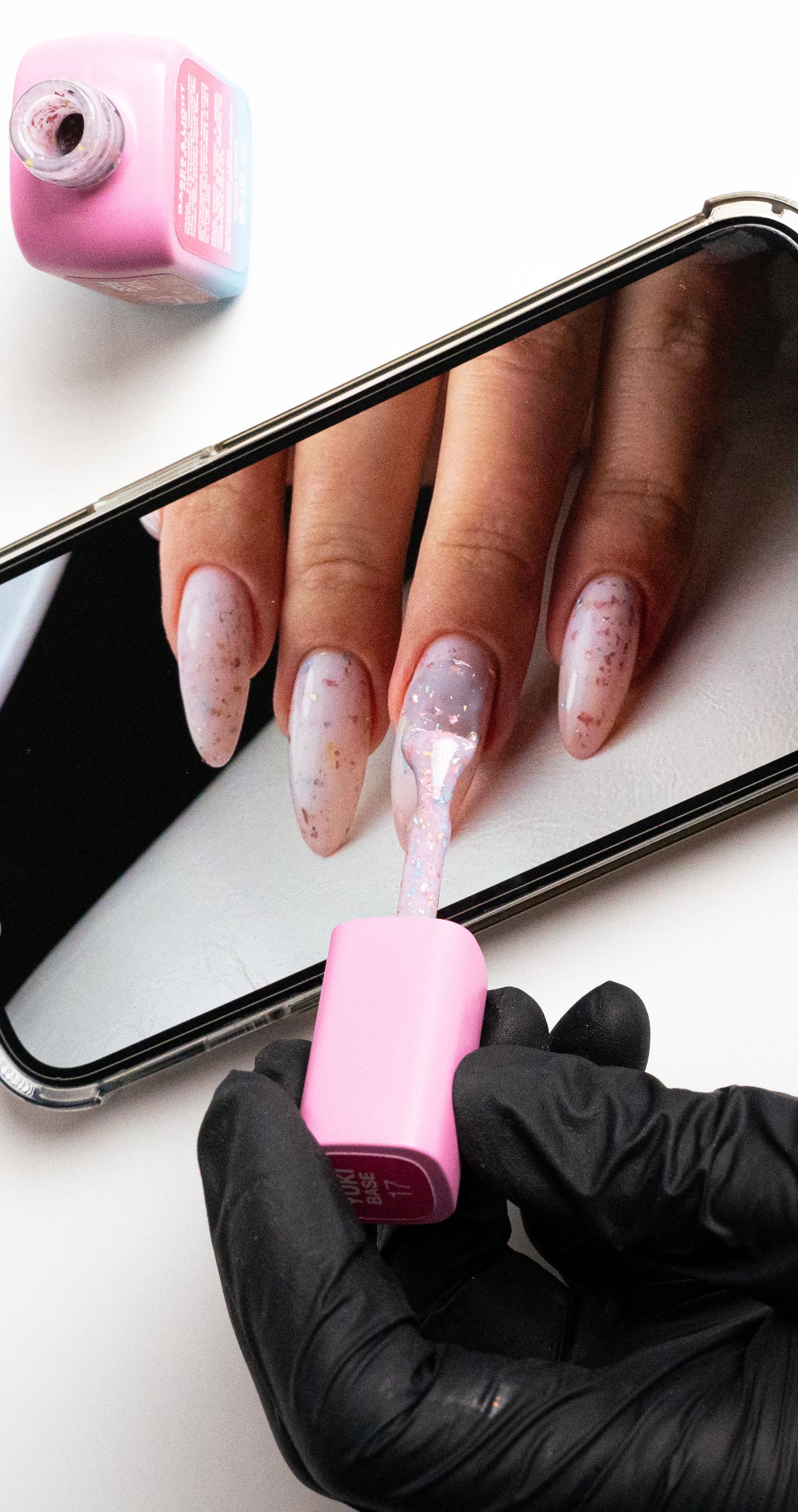 Manicured nails being painted with pink nail polish while resting on smartphone.