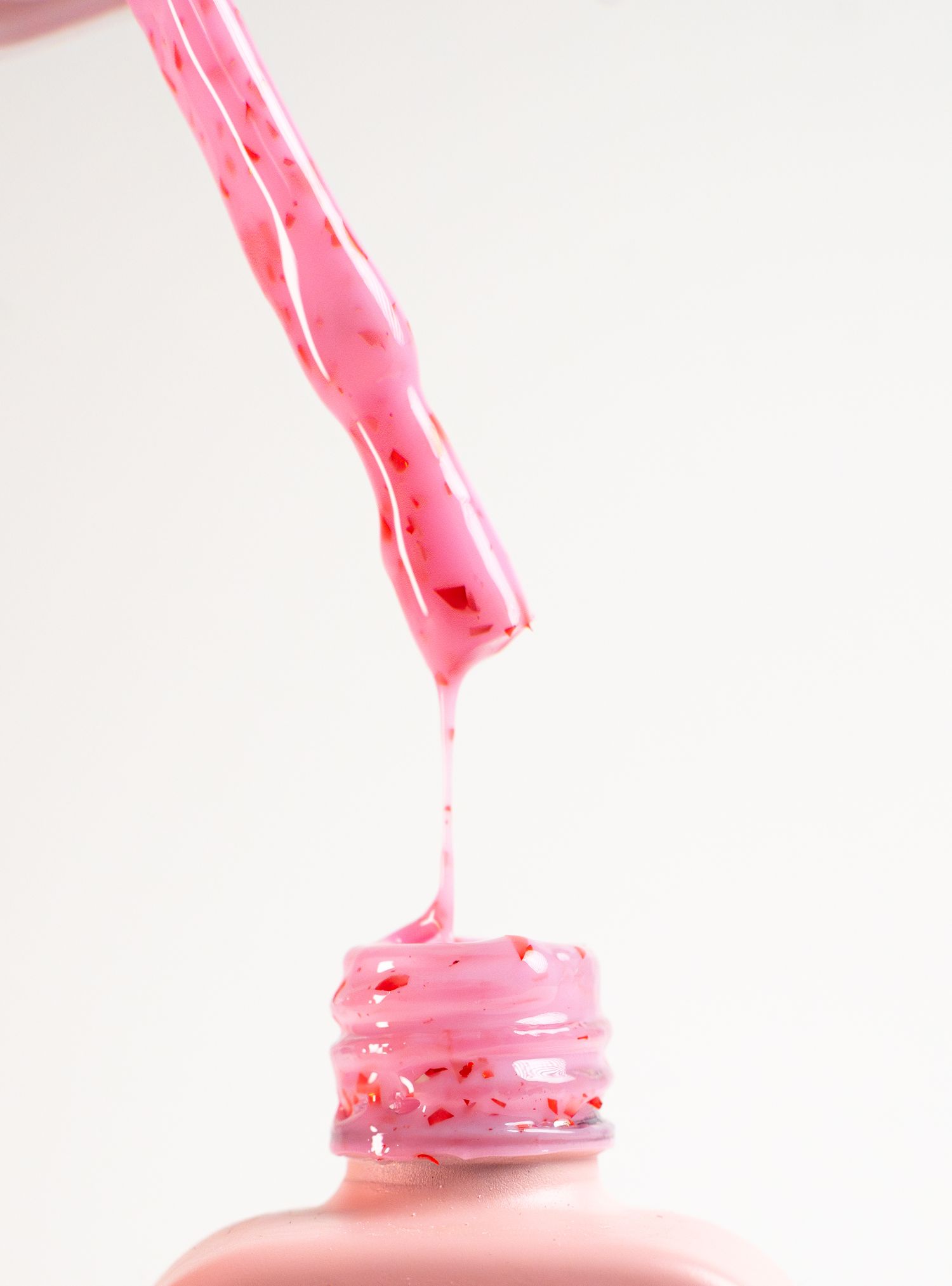 Pink nail polish dripping from bottle brush into container against white background.