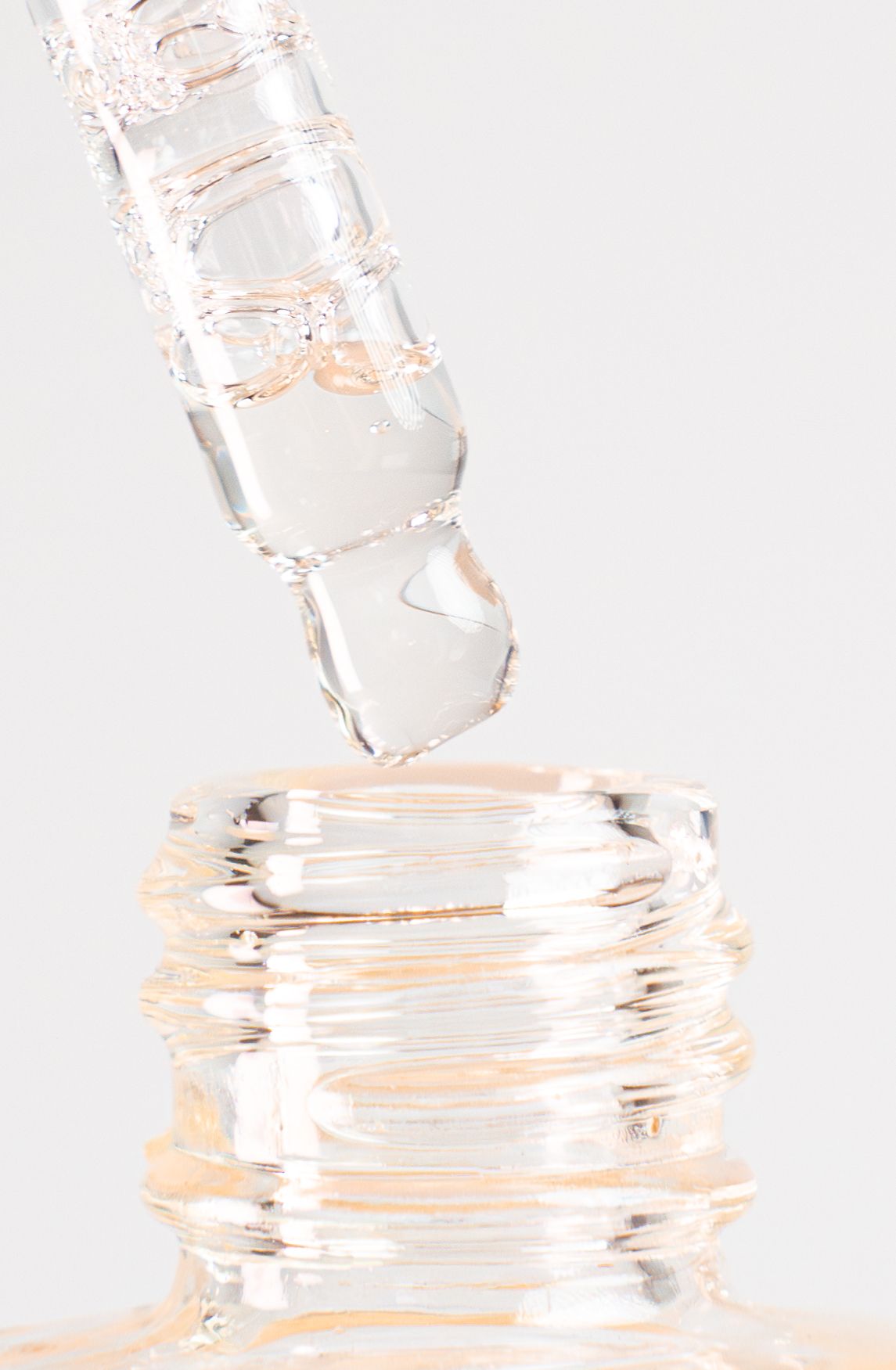 Clear liquid pouring from bottle into container showing rippling effect against white background.