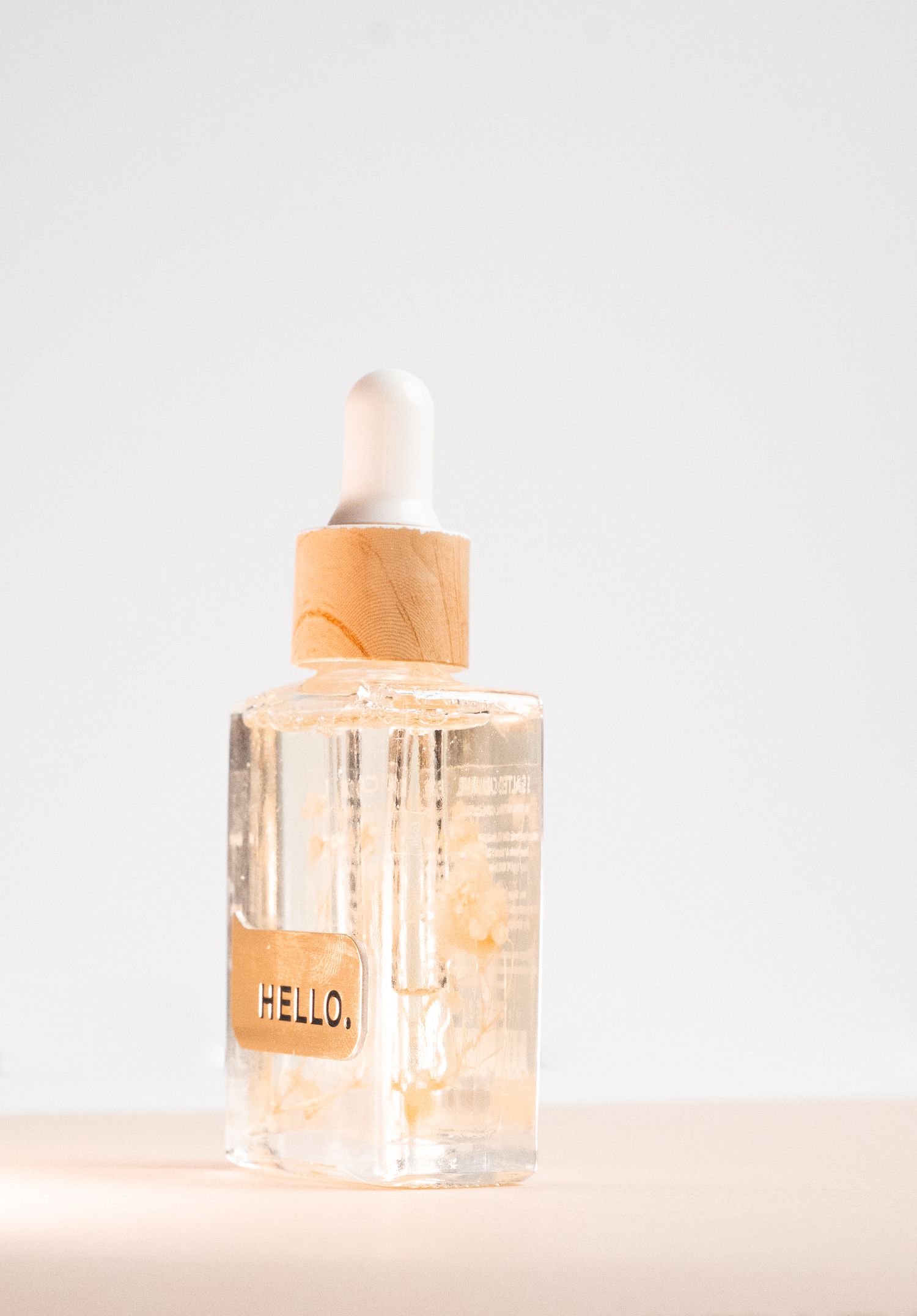 Minimalist glass bottle with wooden cap labeled 'HELLO' against white background.