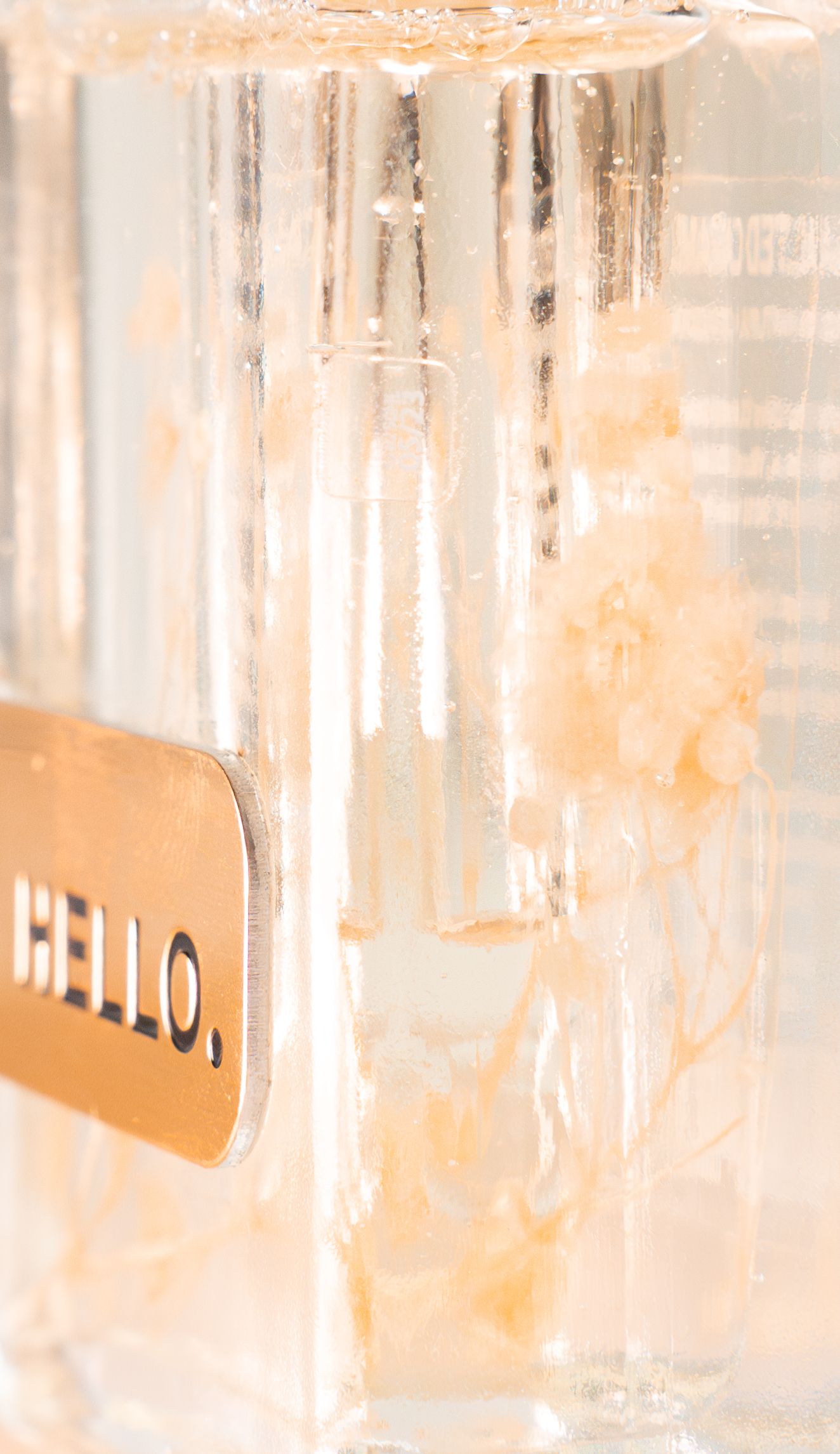Crystal clear glass bottle with 'HELLO' label capturing warm lighting effects.