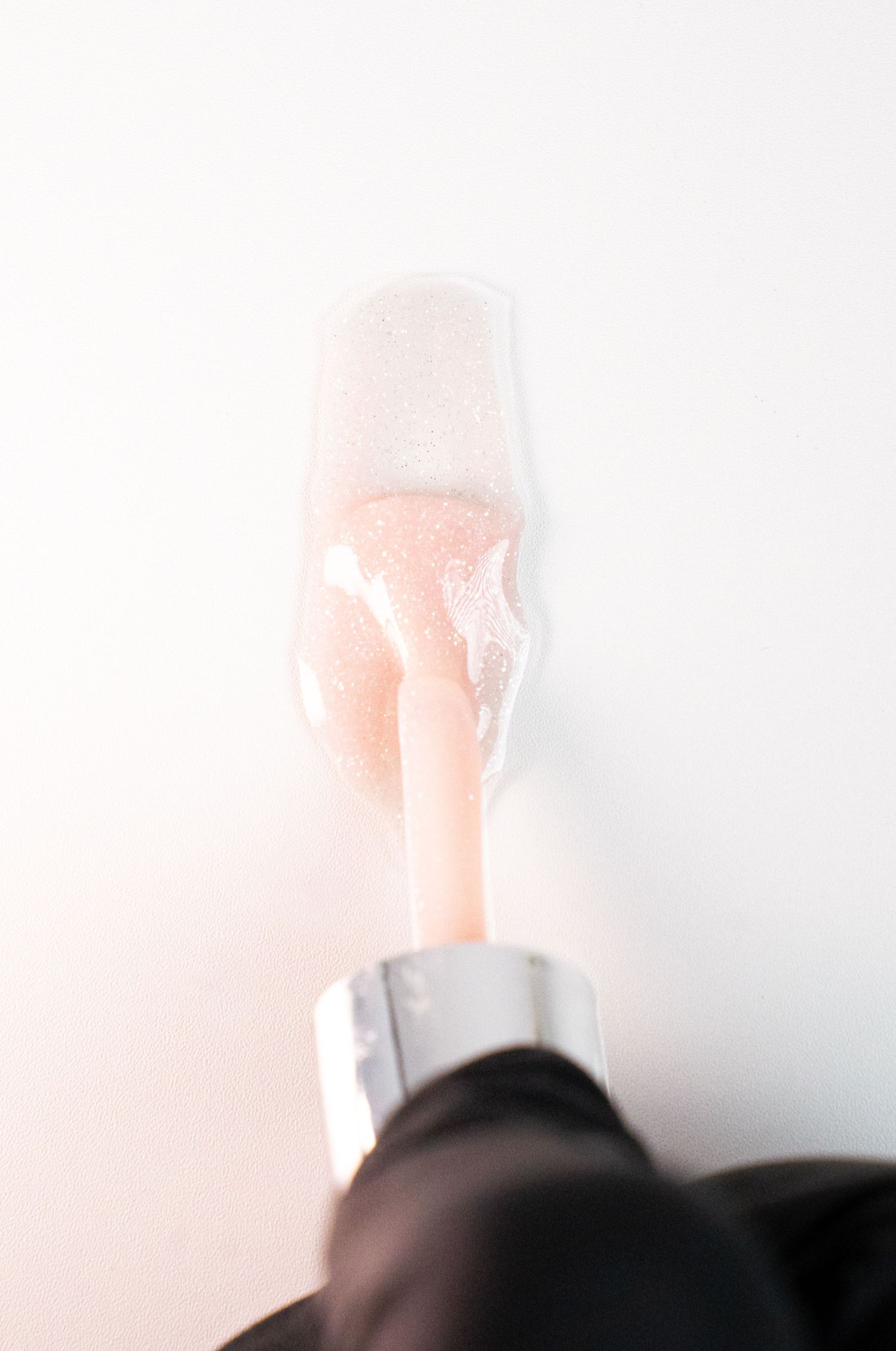 Close-up of nude-colored nail polish brush against white background.