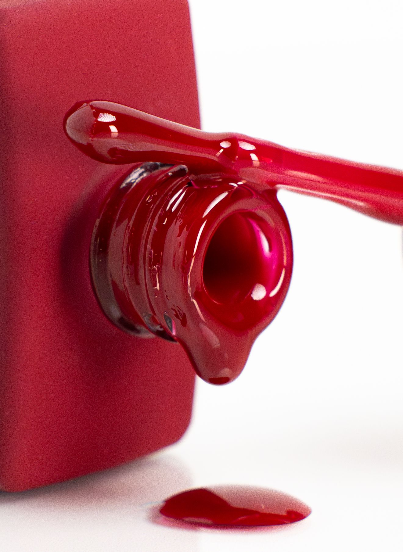 Close-up of red nail polish dripping from brush on bottle neck.