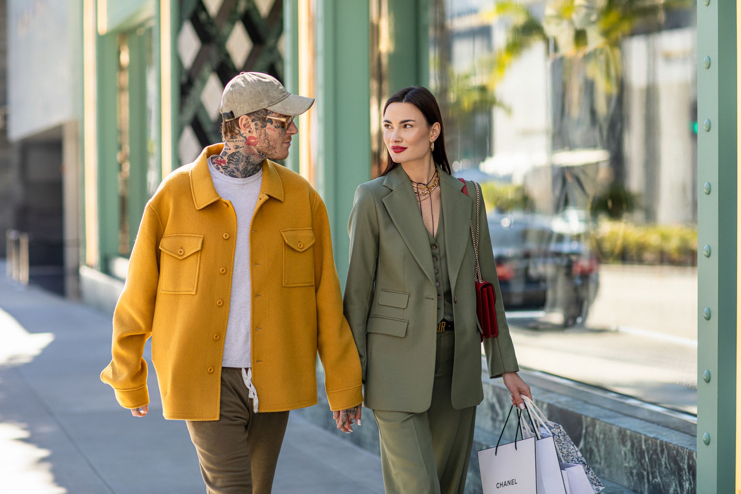 Two people shopping together on a sunny day, one wearing a mustard yellow jacket and another in an olive green suit.