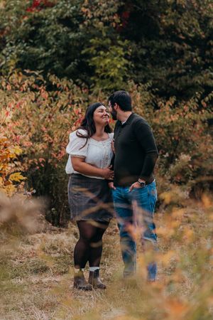 A couple shares romantic moments together in a scenic outdoor setting with autumn foliage in the background.