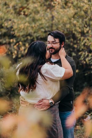 A romantic couple embraces outdoors in an autumn setting with blurred foliage in the foreground.