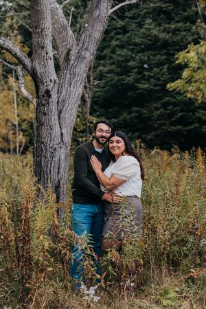 A couple shares a romantic moment among tall wildflowers and trees in a natural outdoor setting.