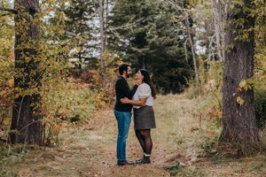 A couple walks together through a scenic autumn forest path surrounded by golden fall foliage.