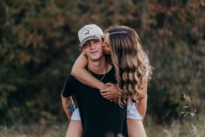 A couple embraces in a romantic outdoor photoshoot with natural lighting and autumn foliage in the background.