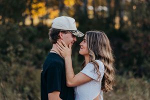 A romantic couple embraces in a golden sunset with autumn trees in the background.