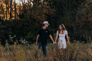 A couple walks through a golden autumn forest at sunset during a romantic outdoor photo session.