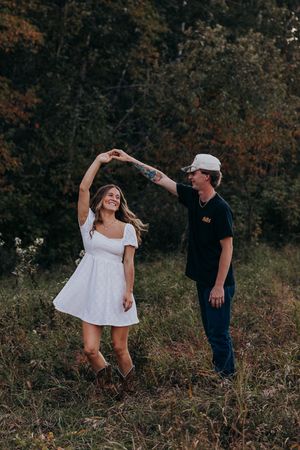 A couple dancing outdoors in autumn, with her wearing a white dress and boots and him in casual dark clothing.