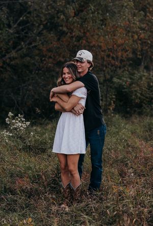A couple shares tender embraces in a natural outdoor setting with autumn foliage in the background.