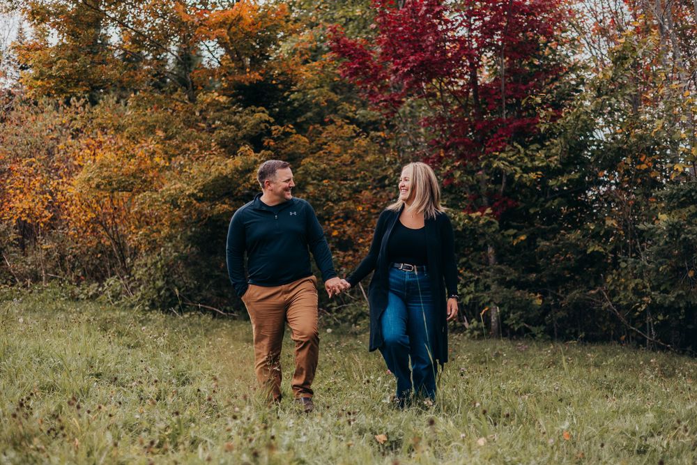 Autumn engagement photo featuring couple walking hand in hand through colorful fall foliage.