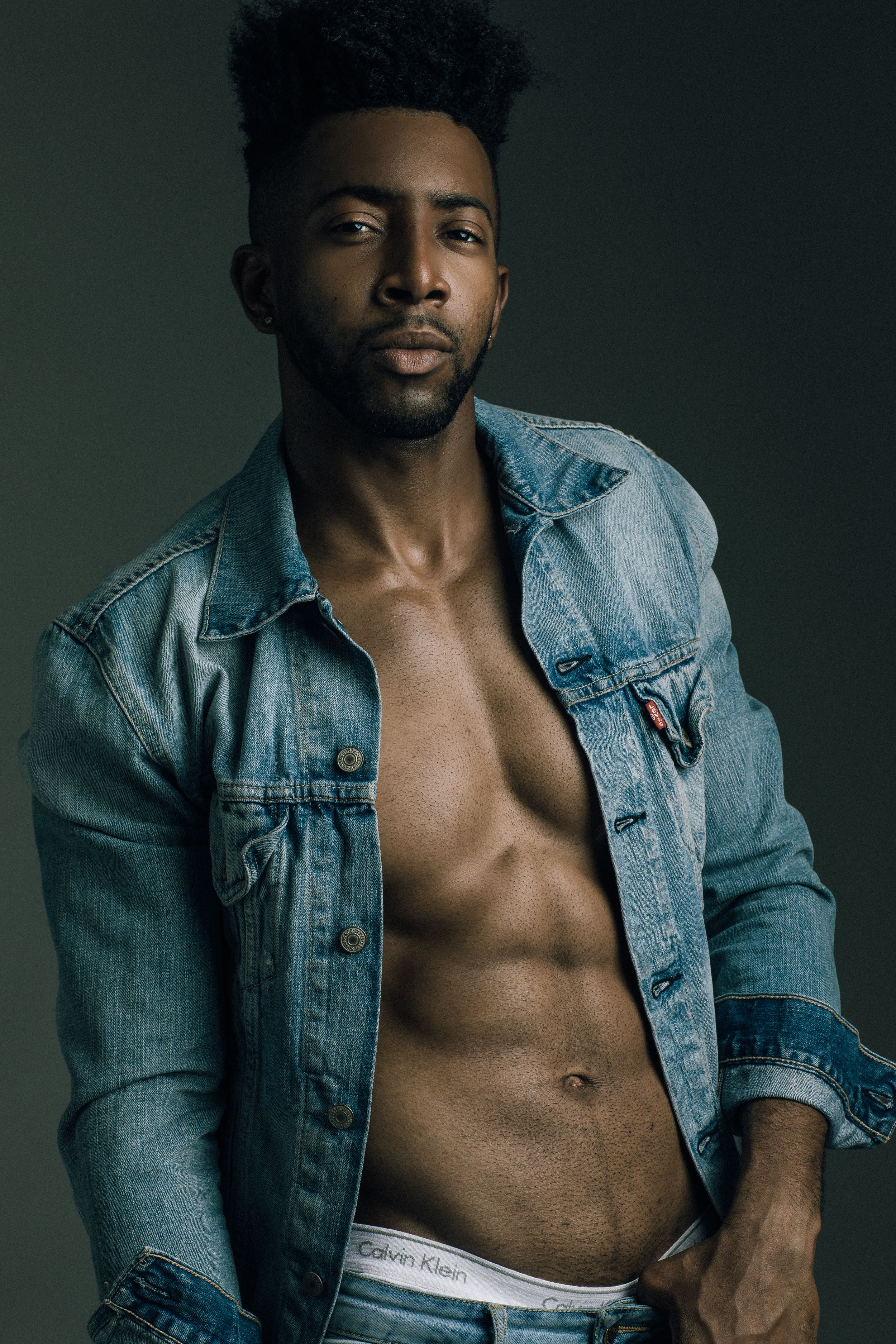 Fashion photo of athletic model in unbuttoned denim jacket against moody backdrop. Shot by Mika Larson Photography.