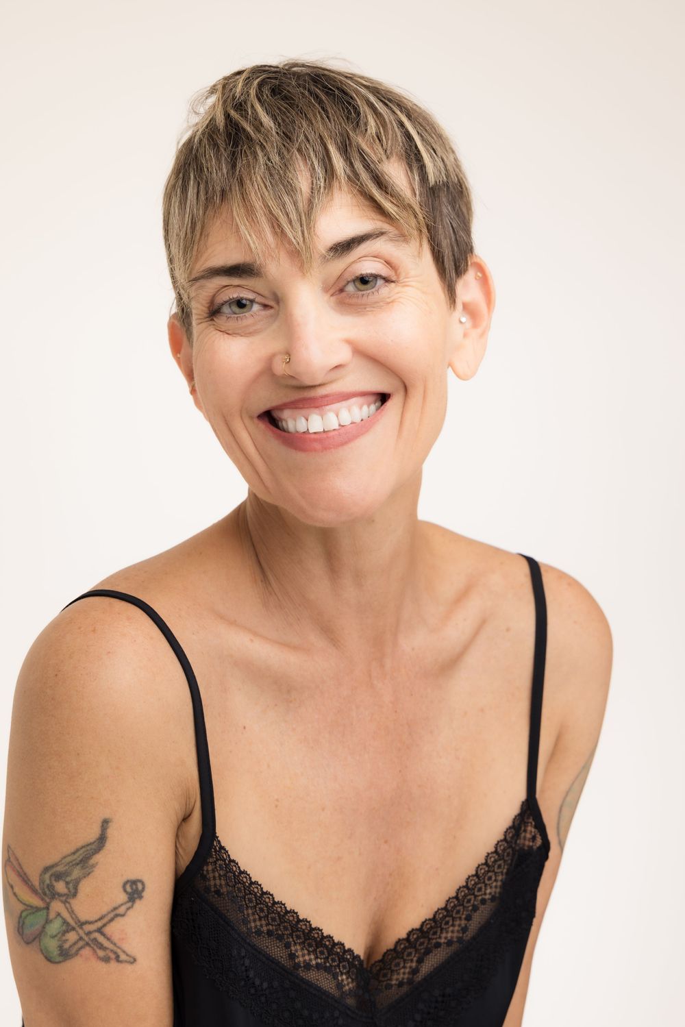 Model headshot of woman with short pixie haircut and visible arm tattoo wearing black camisole. Shot by Mika Larson Photography.
