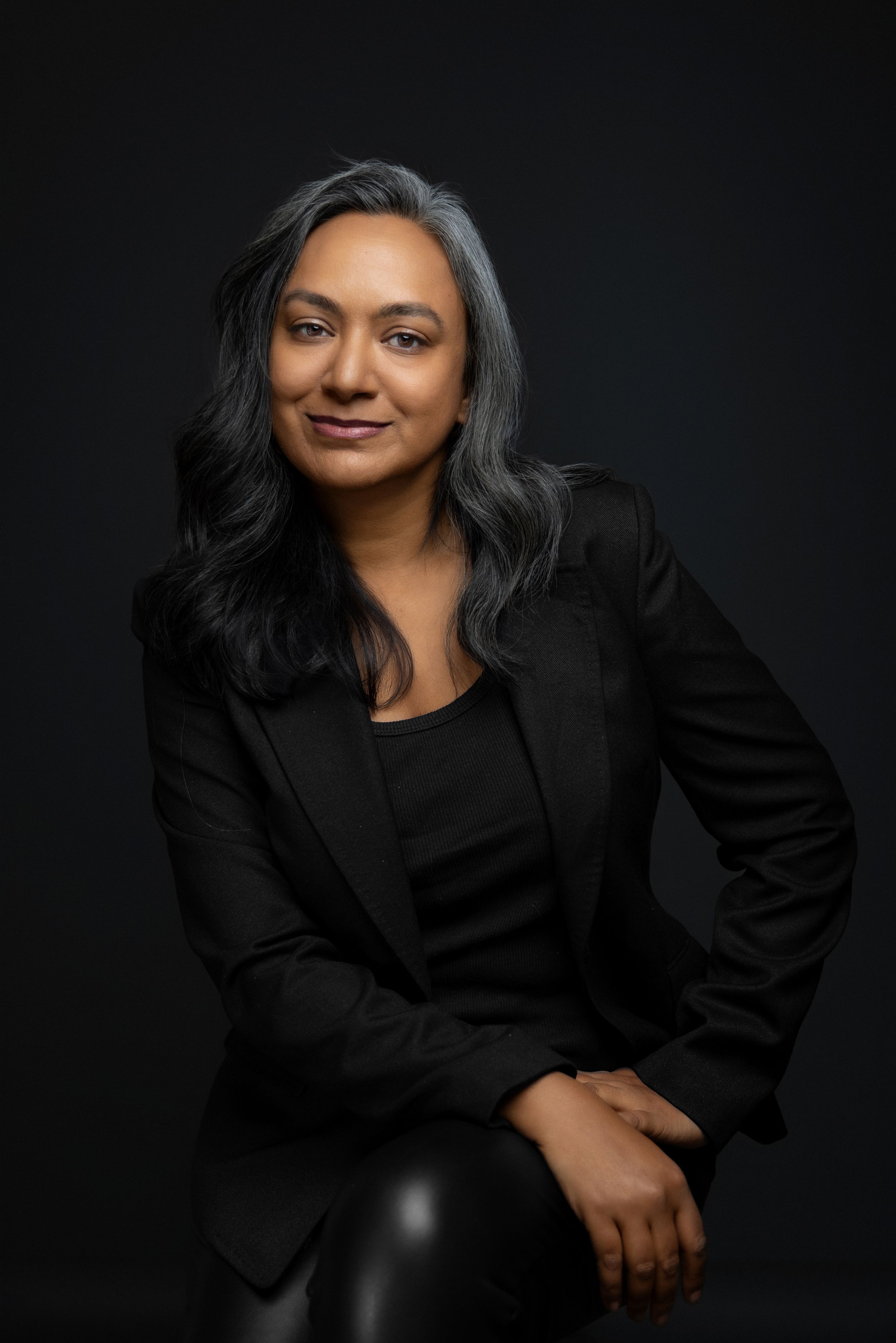 Director headshot of woman in black blazer against dark background with silver streaked hair. Shot by Mika Larson Photography.