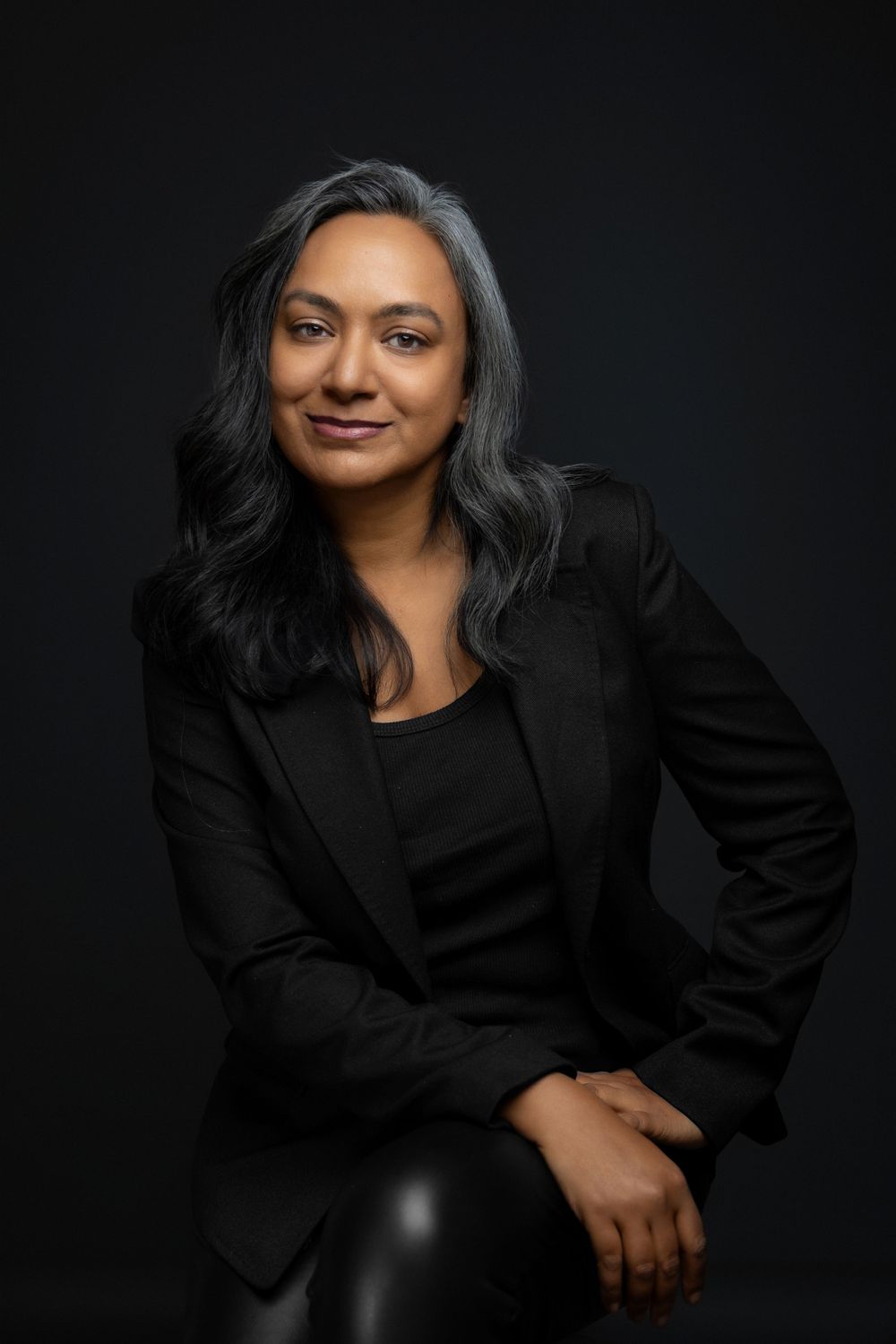 Director headshot of woman in black blazer against dark background with silver streaked hair. Shot by Mika Larson Photography.