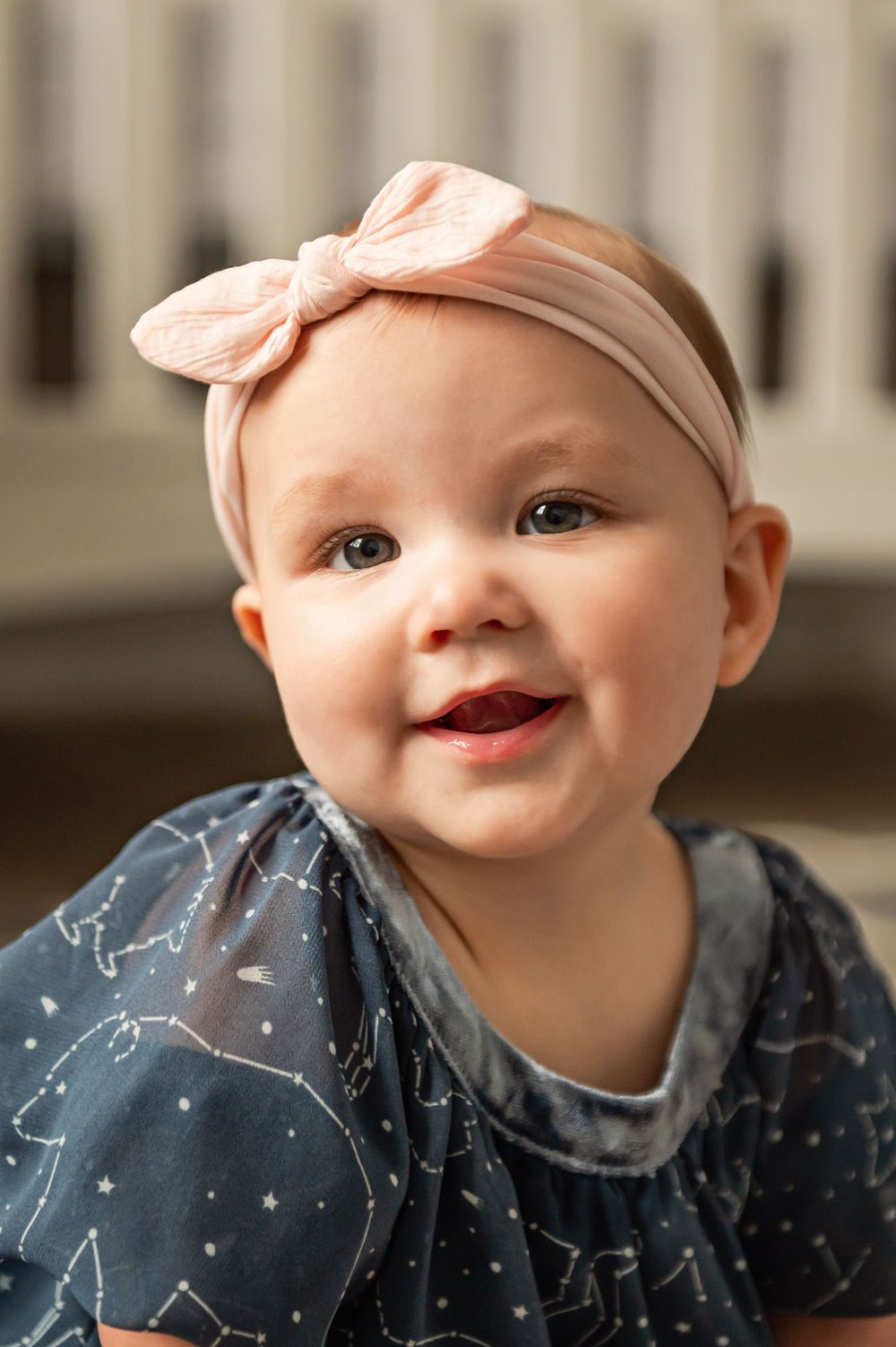 Baby wearing constellation print outfit and pink bow headband smiling brightly.