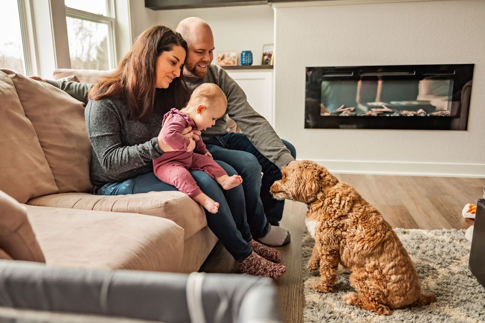Family relaxing on couch with their goldendoodle dog by fireplace.