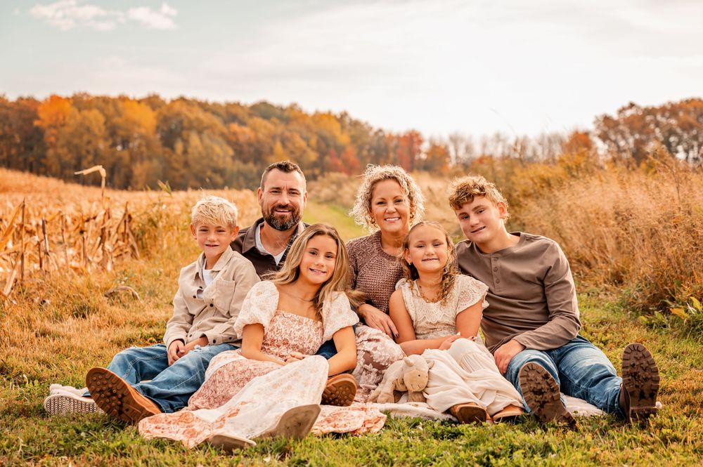 A group of people relaxing together on a blanket in a golden autumn field during sunset.