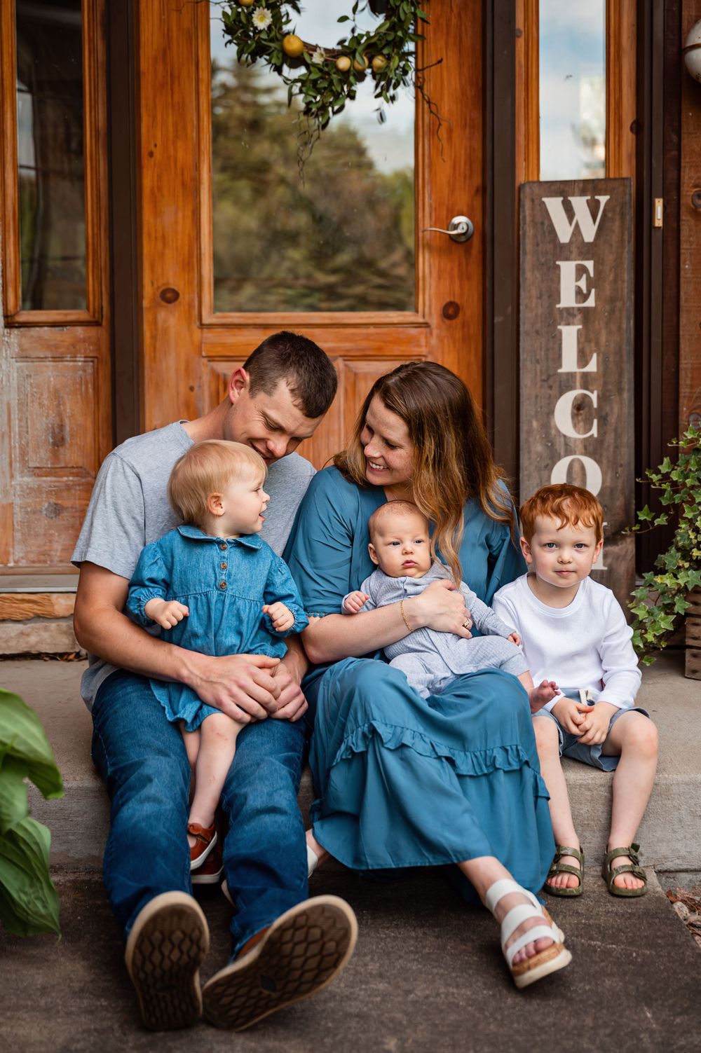 A family sits together on their front porch next to a welcome sign.