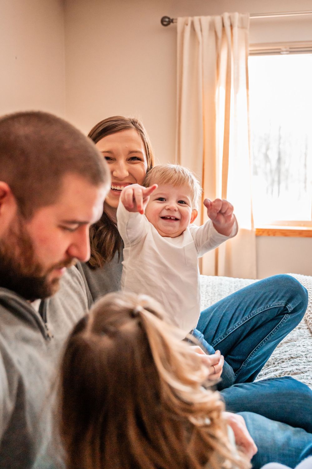 Candid family moment sharing laughs together on bed by window.