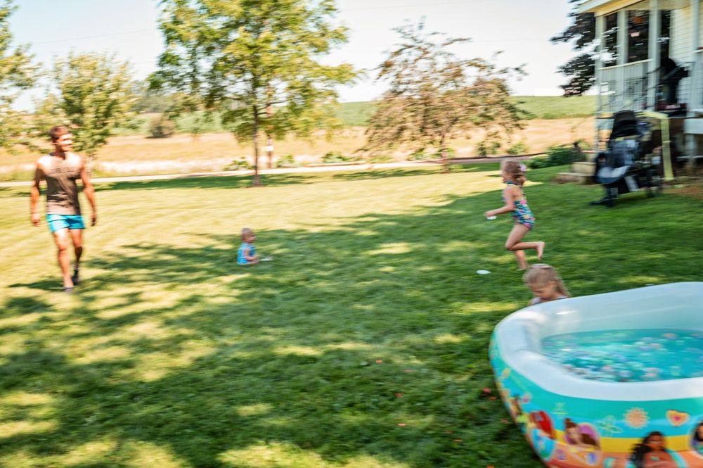 Children play near inflatable pool on sunny summer lawn.
