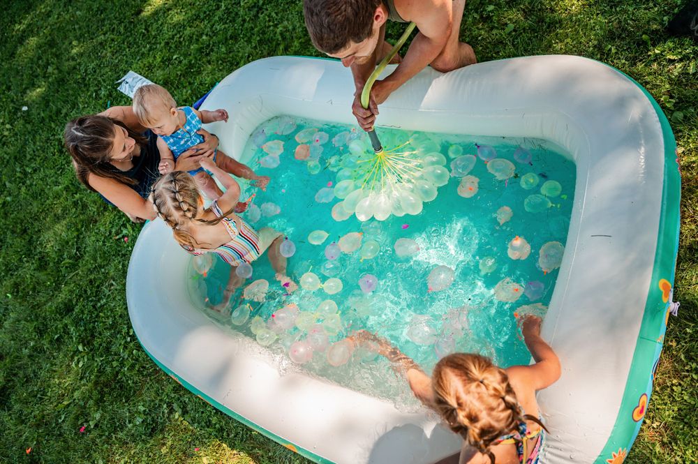 Children enjoying summer fun in a heart-shaped inflatable pool with turquoise water and floating toys.