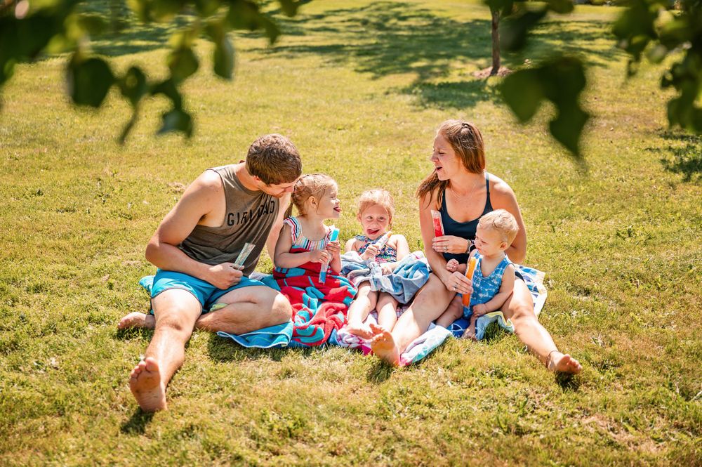 Family relaxing together on a blanket in a sunny grassy field.