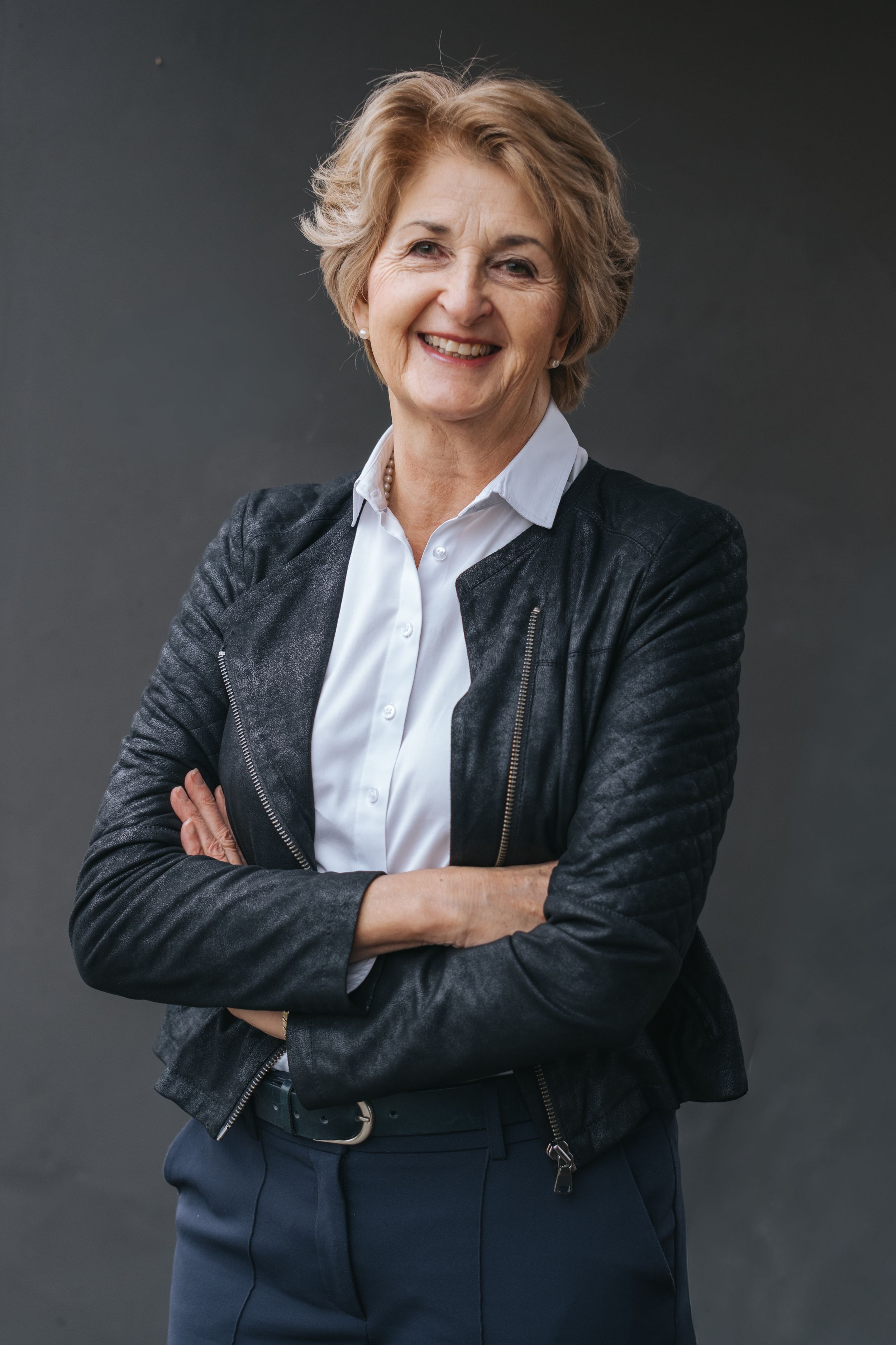 Businessporträt: Frau mit verschränkten Armen vor dunklem Hintergrund, natürliches Porträt im Studio.