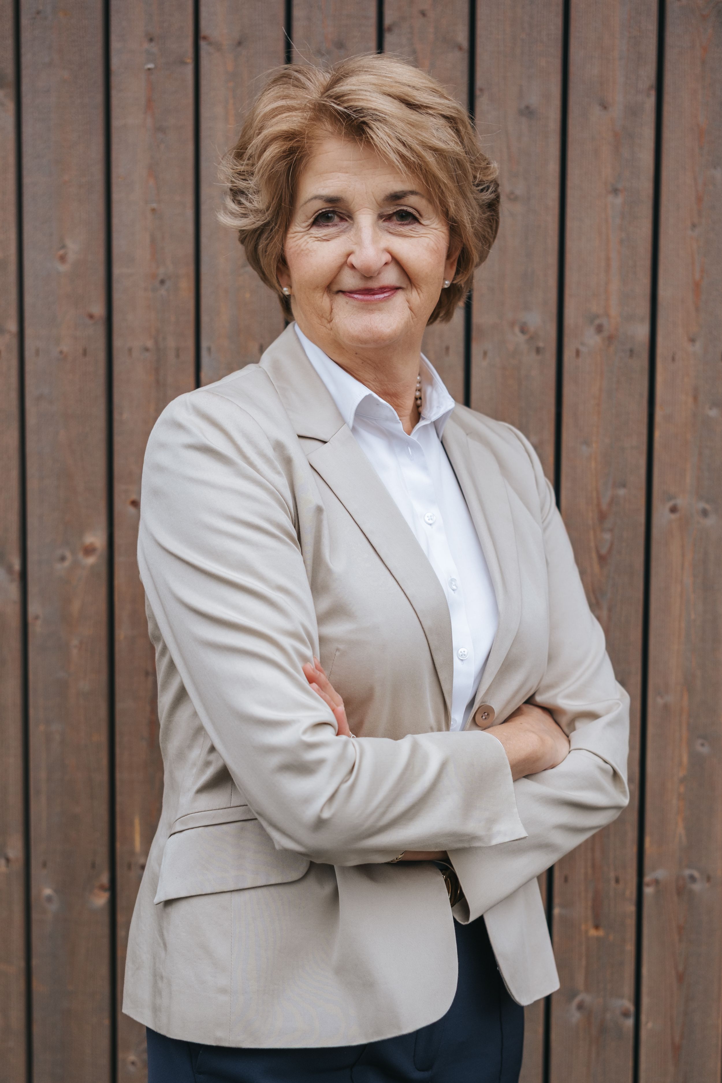 Businessporträt: Frau steht vor einer Holzfassade mit verschränkten Armen und blickt selbstbewusst in die Kamera.