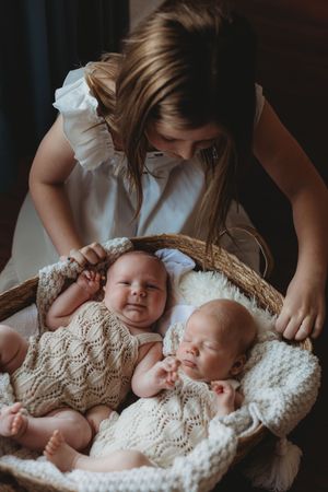 Two sleeping newborn babies in knitted outfits rest in a woven basket with soft blankets.