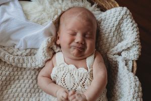 Newborn baby sleeping peacefully in white knitted blanket with natural lighting in vintage style photography.