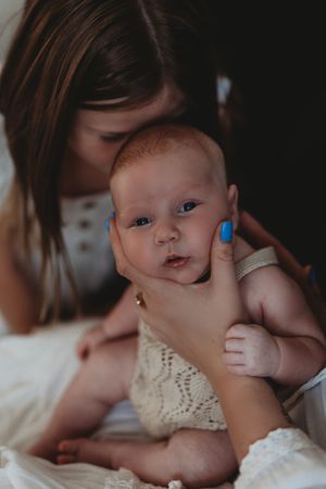 Baby in white lace dress being cradled close while nursing in dark moody lighting.