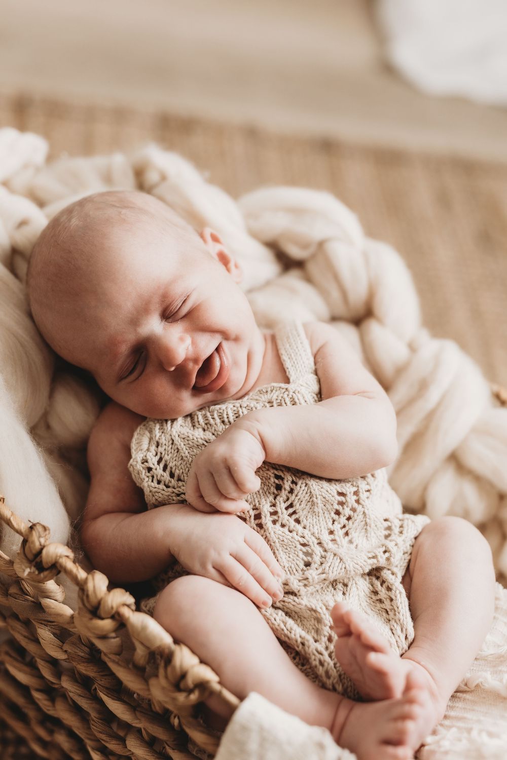 Sleeping newborn baby photographed on textured beige blanket in natural light.