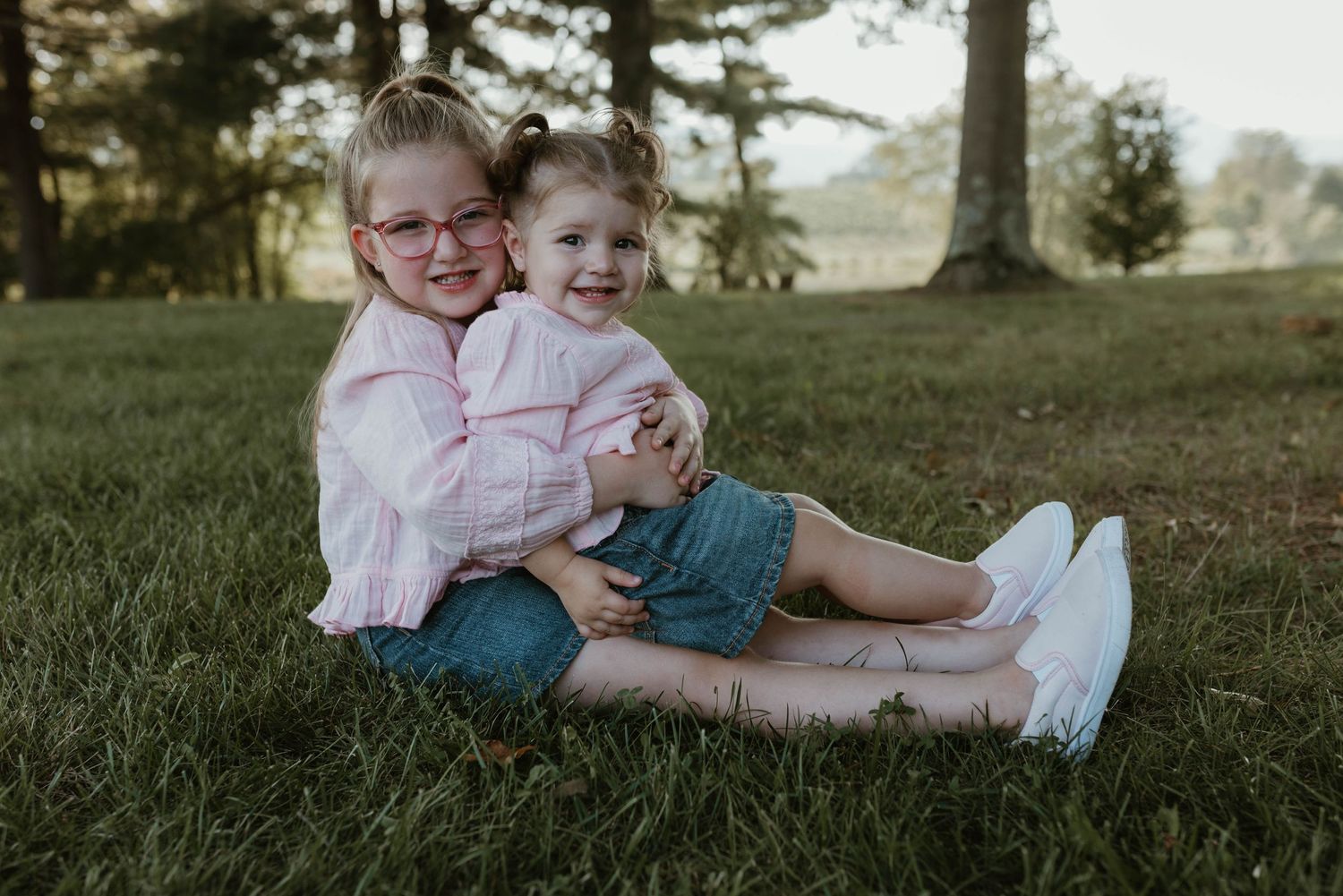 Two children playing and laughing together on grassy hillside during outdoor photo session.