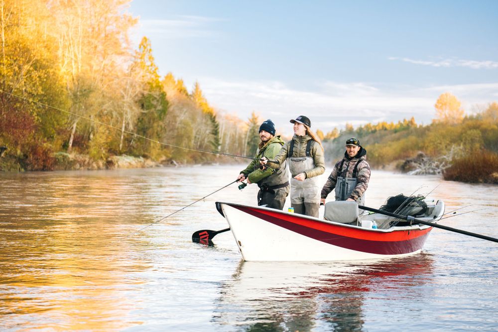 Three anglers fishing from small motorboat on autumn river during golden hour.