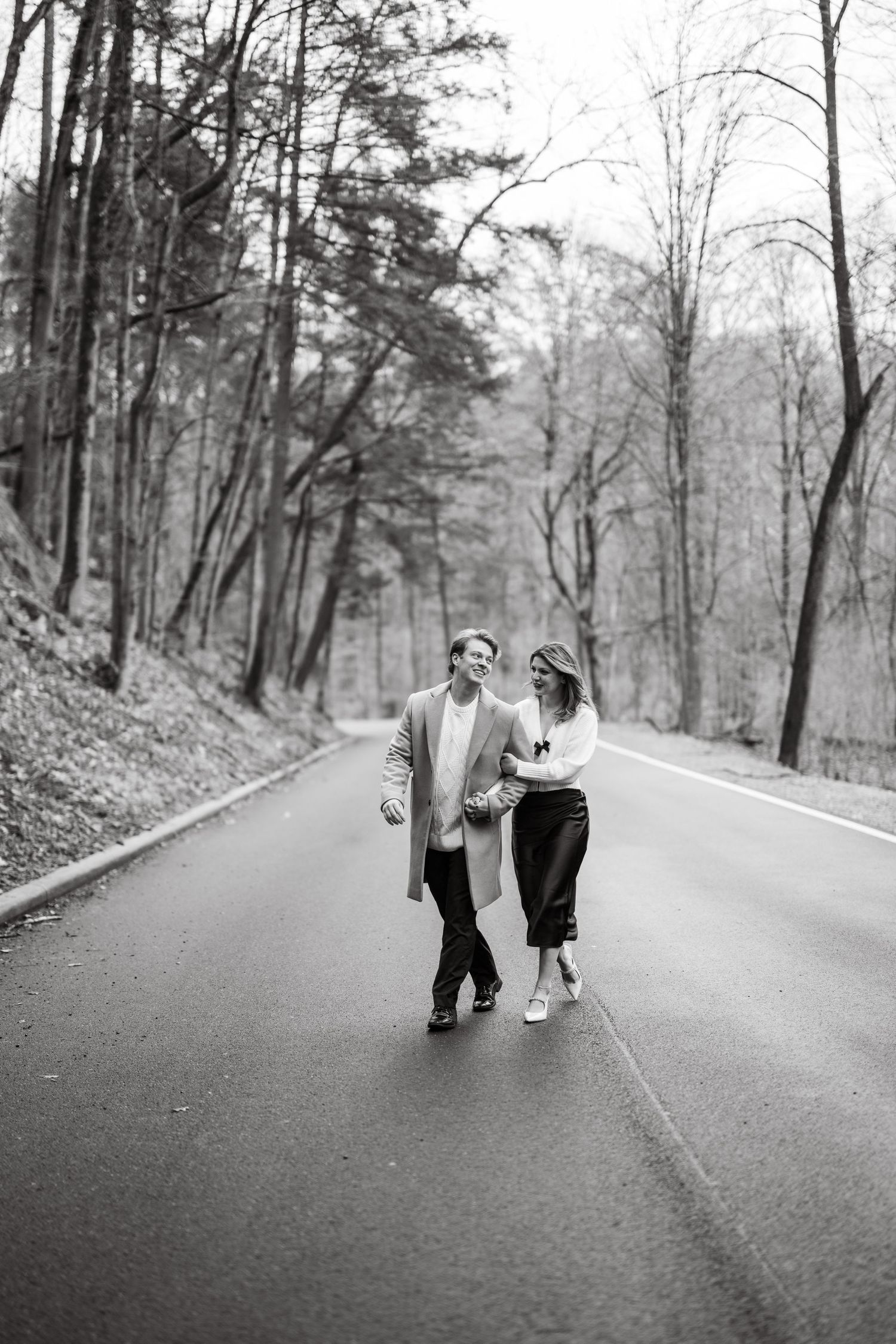 A couple takes a romantic stroll together down a tree-lined road on a misty day in black and white photography.