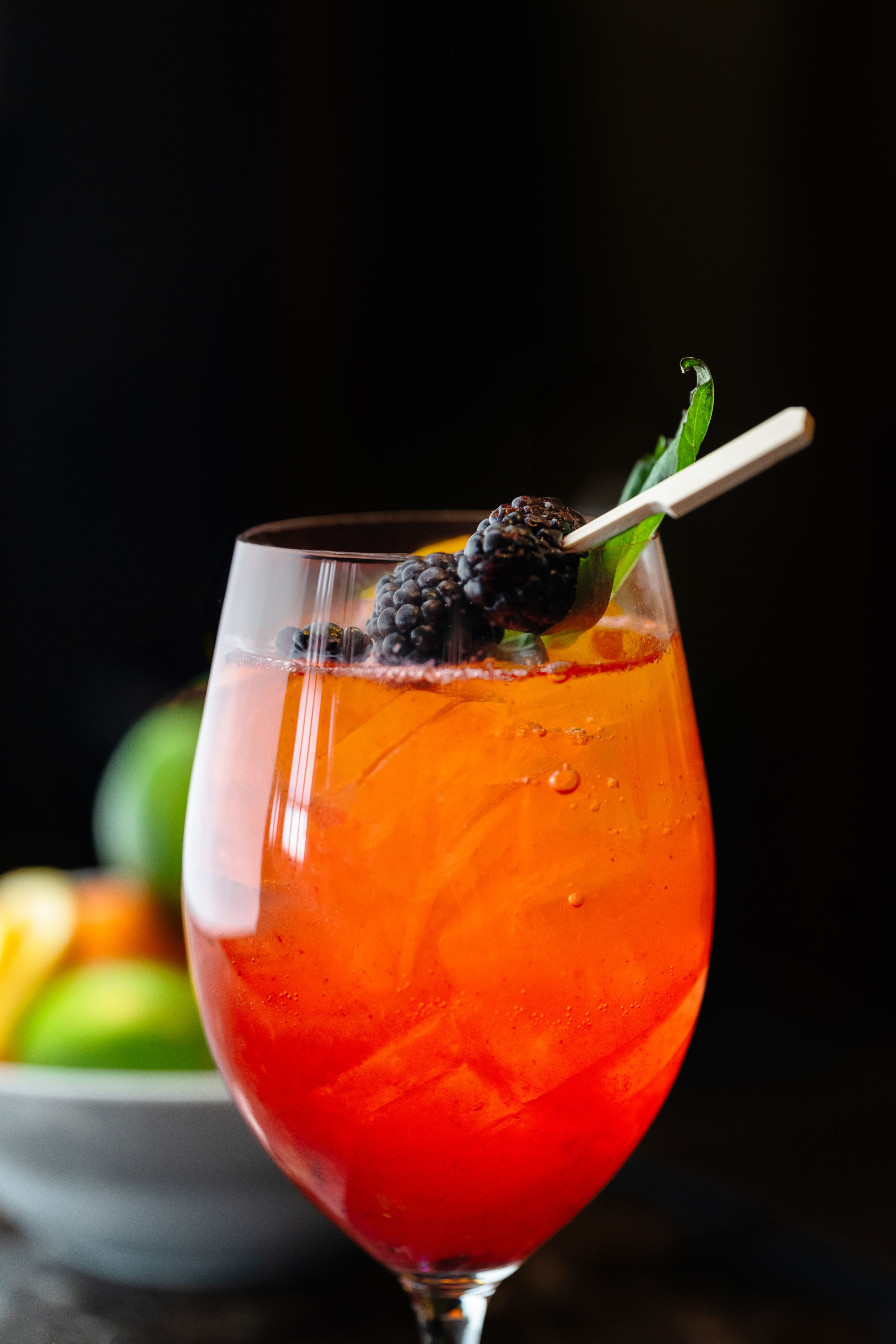 Vibrant orange cocktail garnished with blackberries and herbs in a wine glass.