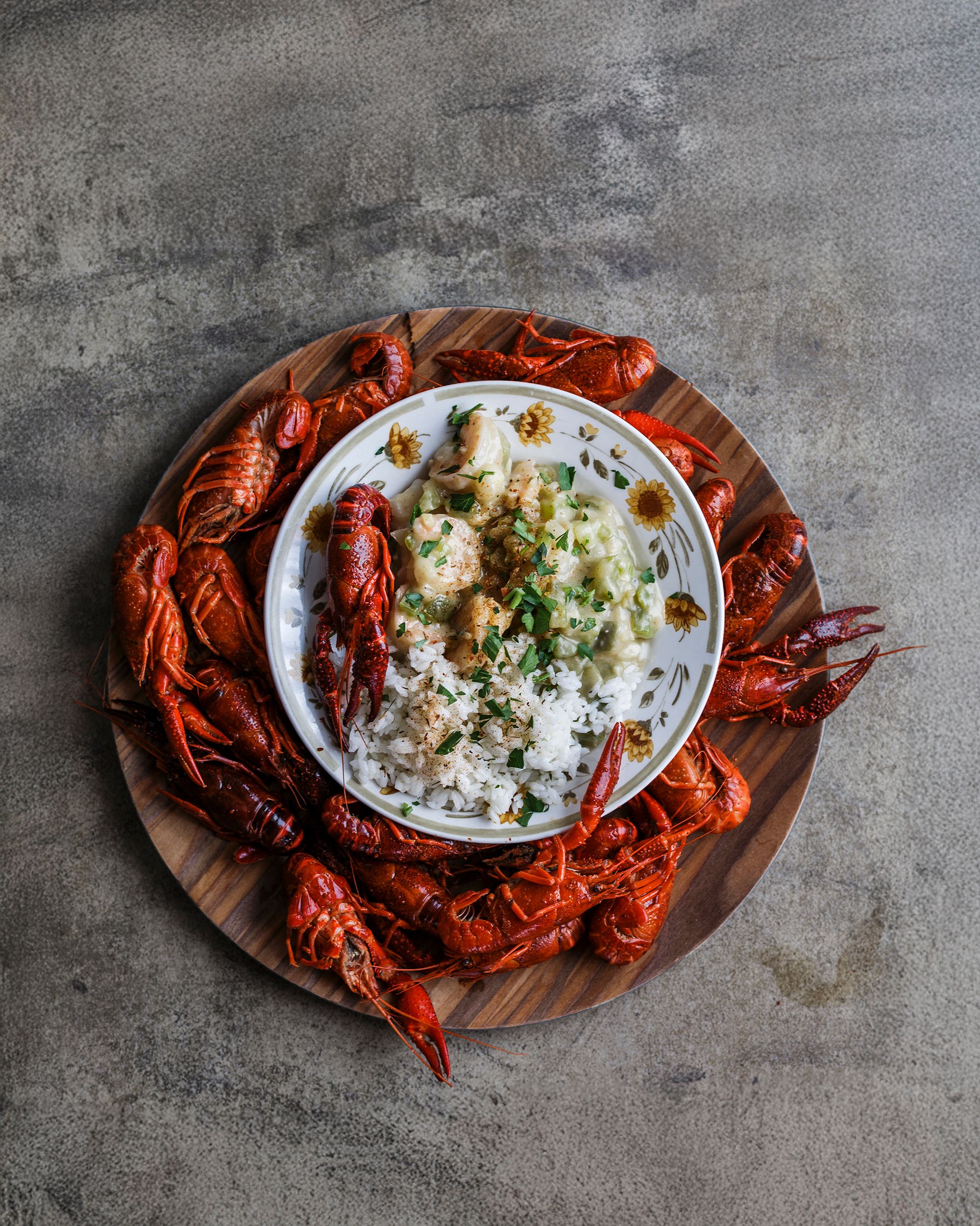 Top down view of a creamy seafood dip surrounded by bright red cooked crawfish on a wooden board.