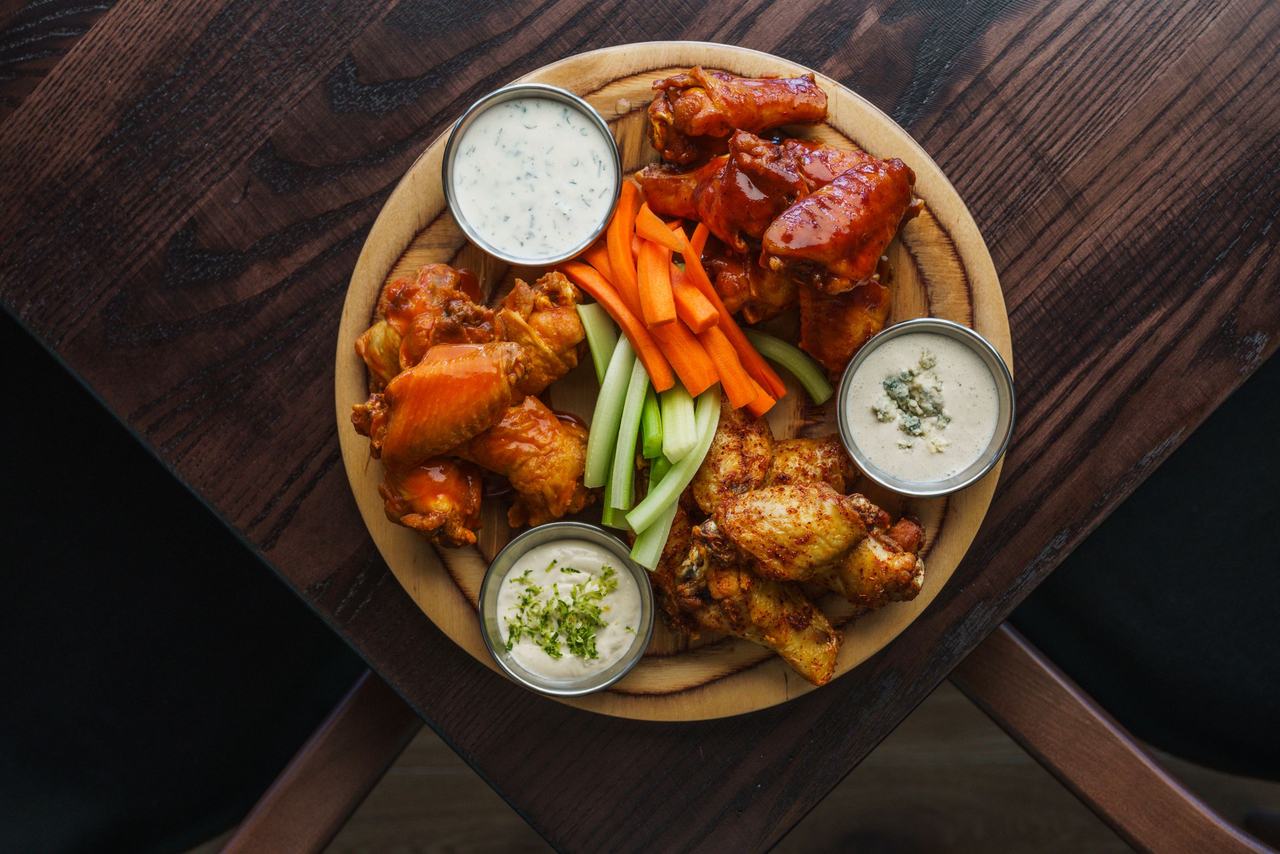 Plate of spicy chicken wings served with celery sticks and dipping sauces on wooden table.