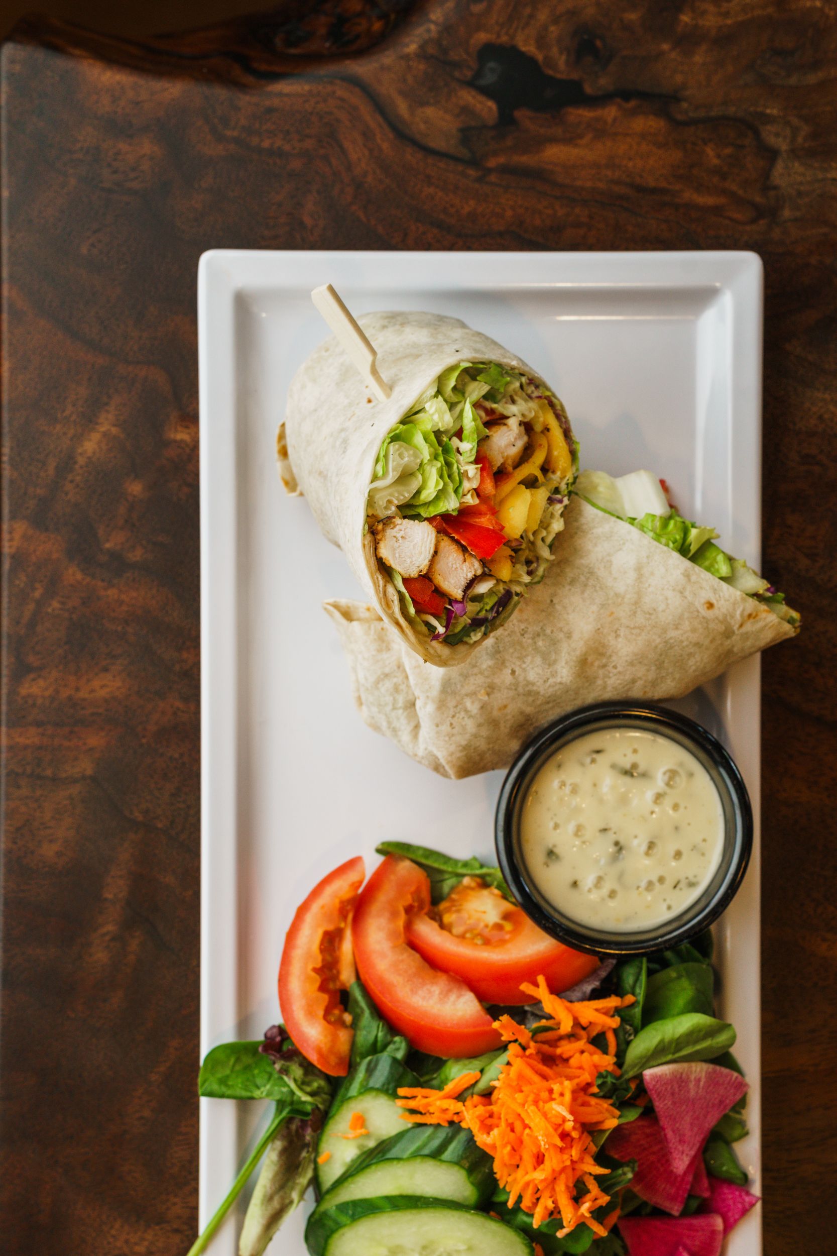 Wrap sandwich served with fresh garden salad and creamy dipping sauce on white plate.