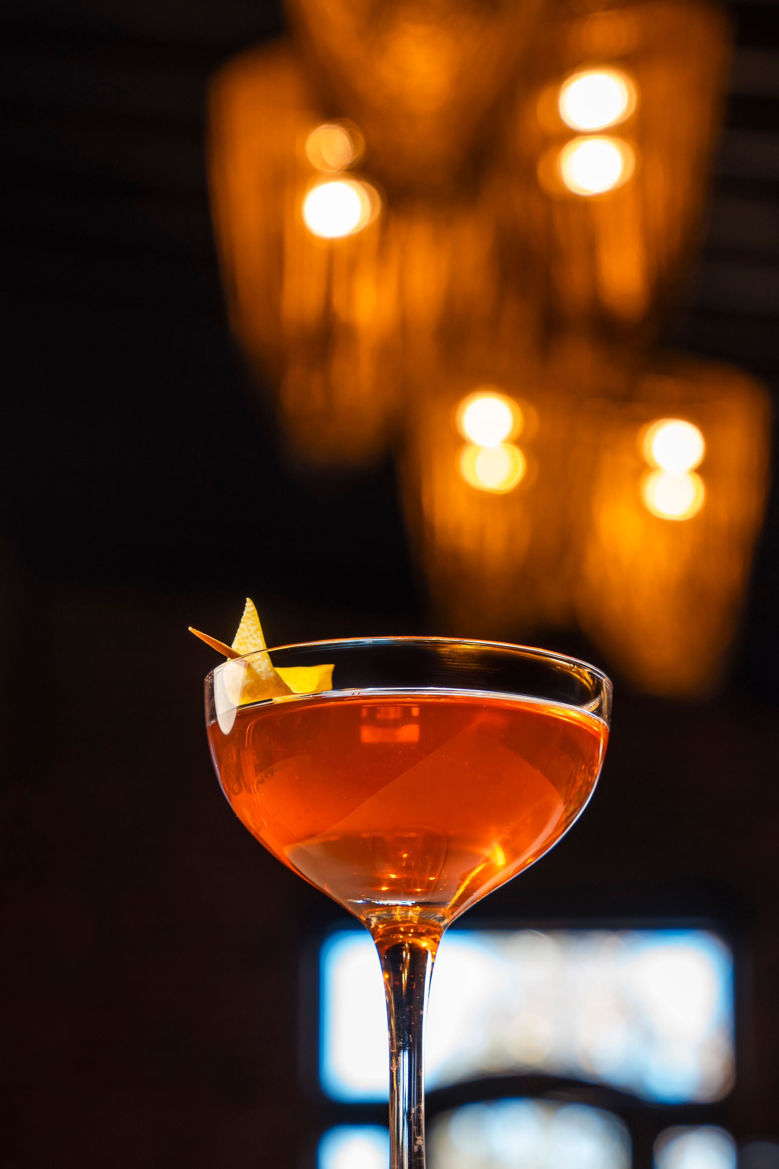 Elegant cocktail in coupe glass garnished with star-shaped citrus peel against warm glowing candlelit background.