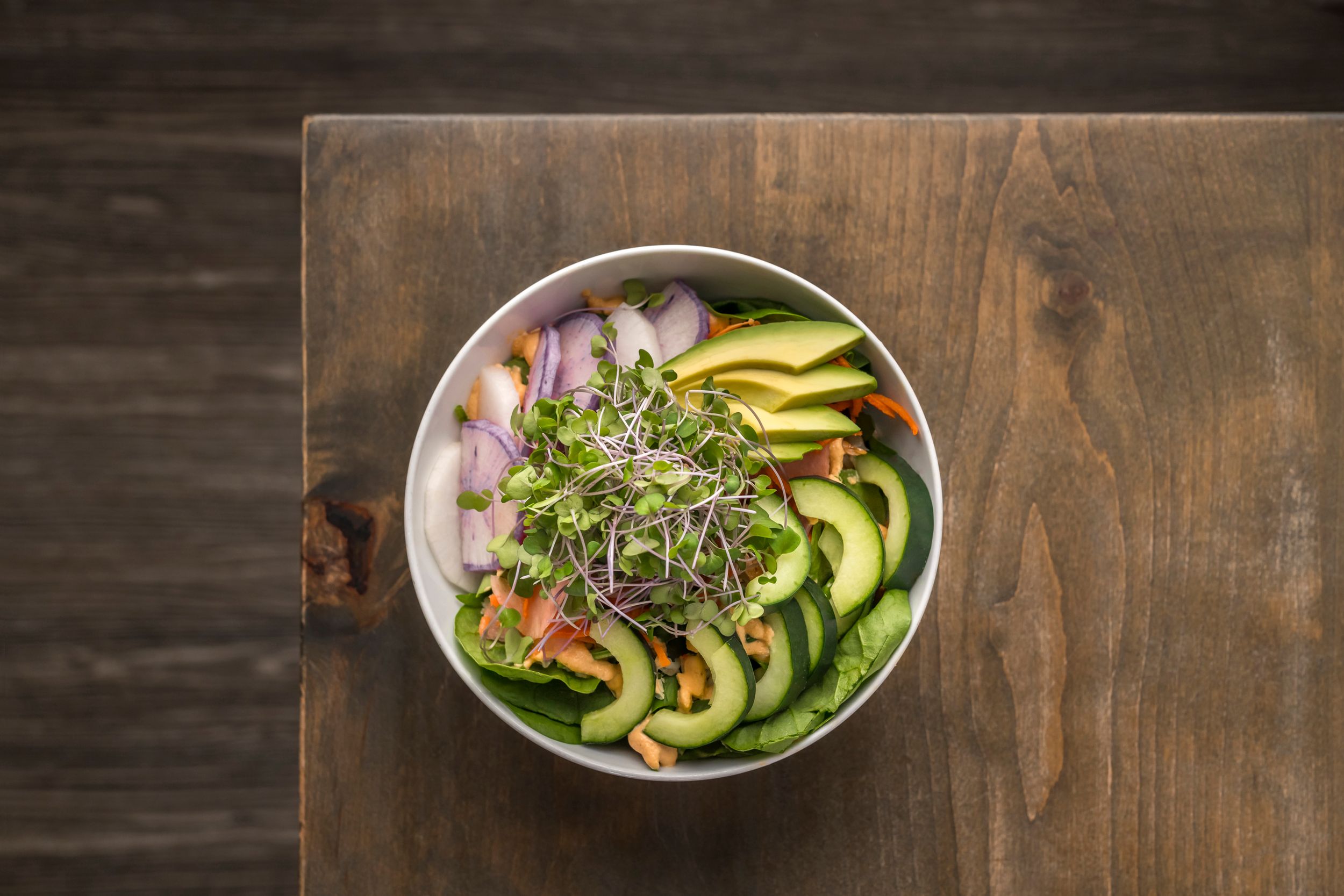 Fresh poke bowl with sliced avocado, microgreens and raw fish served on wooden table.