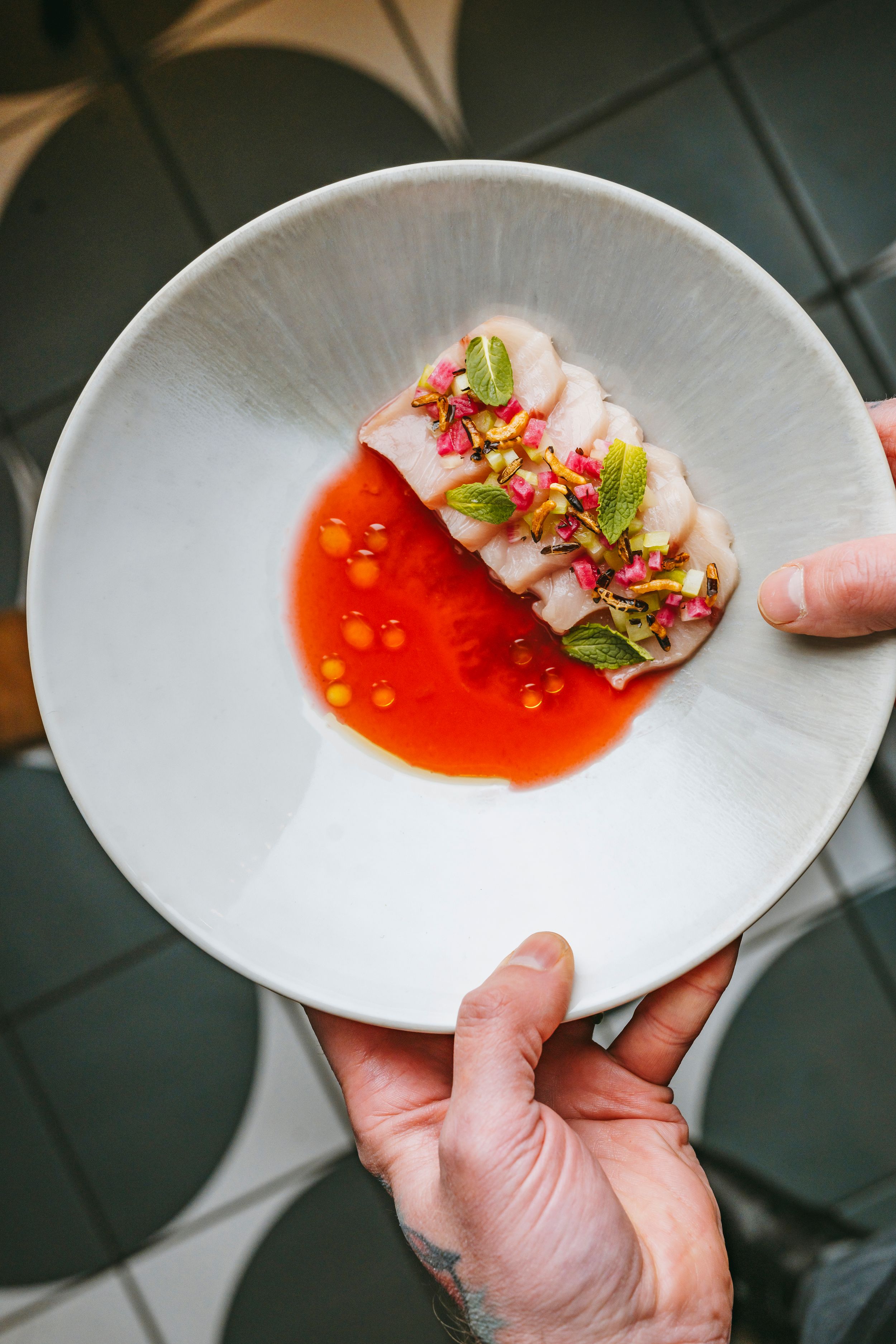 Whitefish dish plated with bright red sauce and microgreens on a ceramic plate.