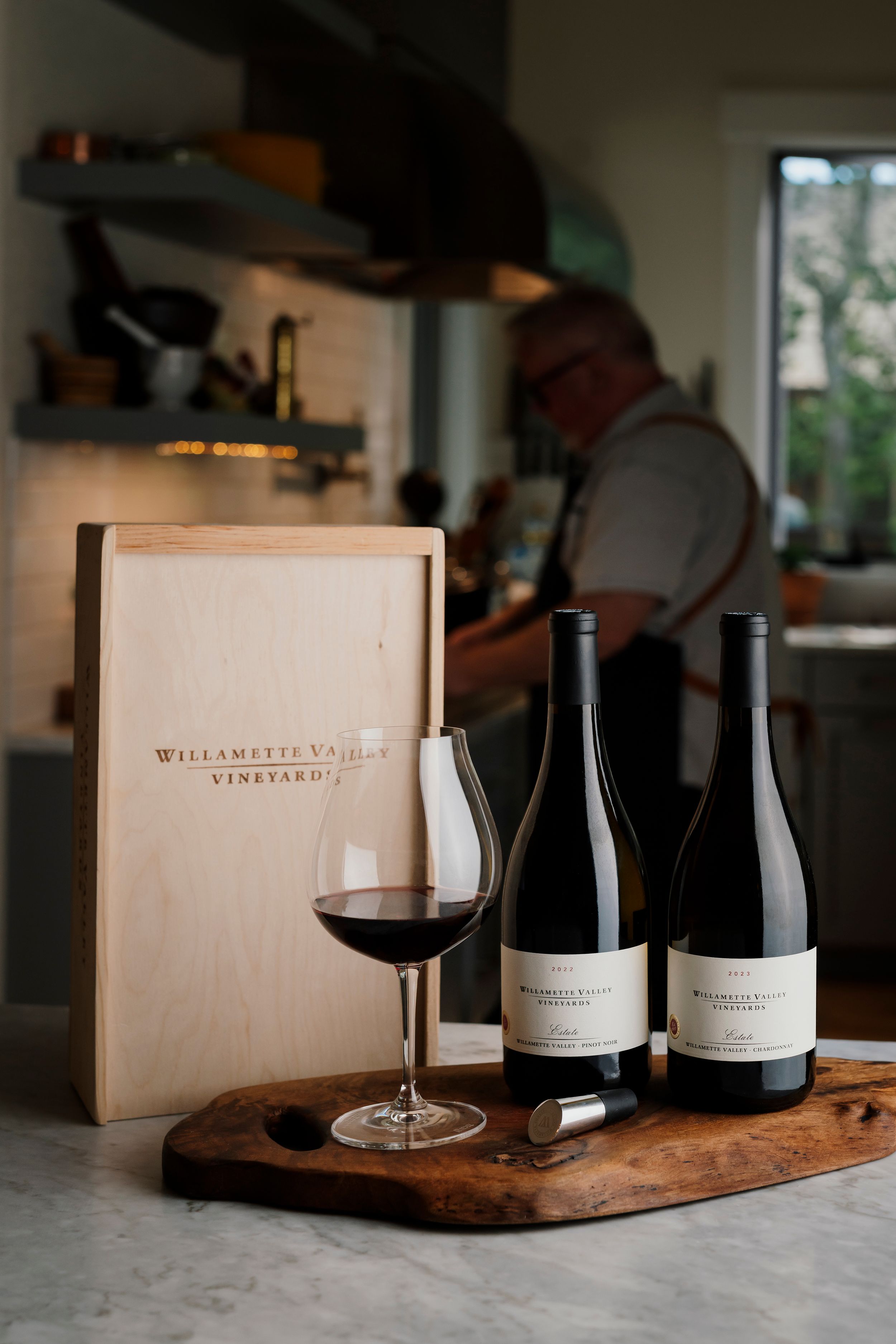 Two bottles of red wine with a glass and wooden box from Willamette Valley Vineyards on rustic wooden serving board.