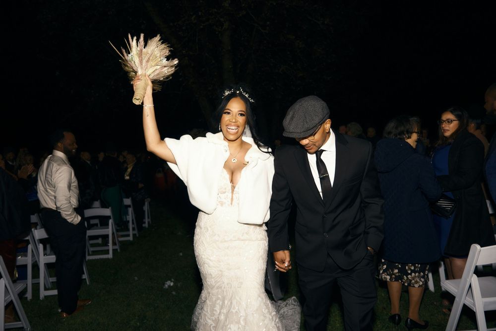 Celebratory moment at outdoor evening wedding as couple walks among white chairs.