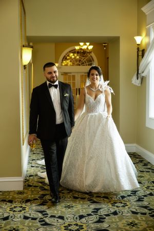 An elegant couple walking through an ornate hallway in formal wedding attire.