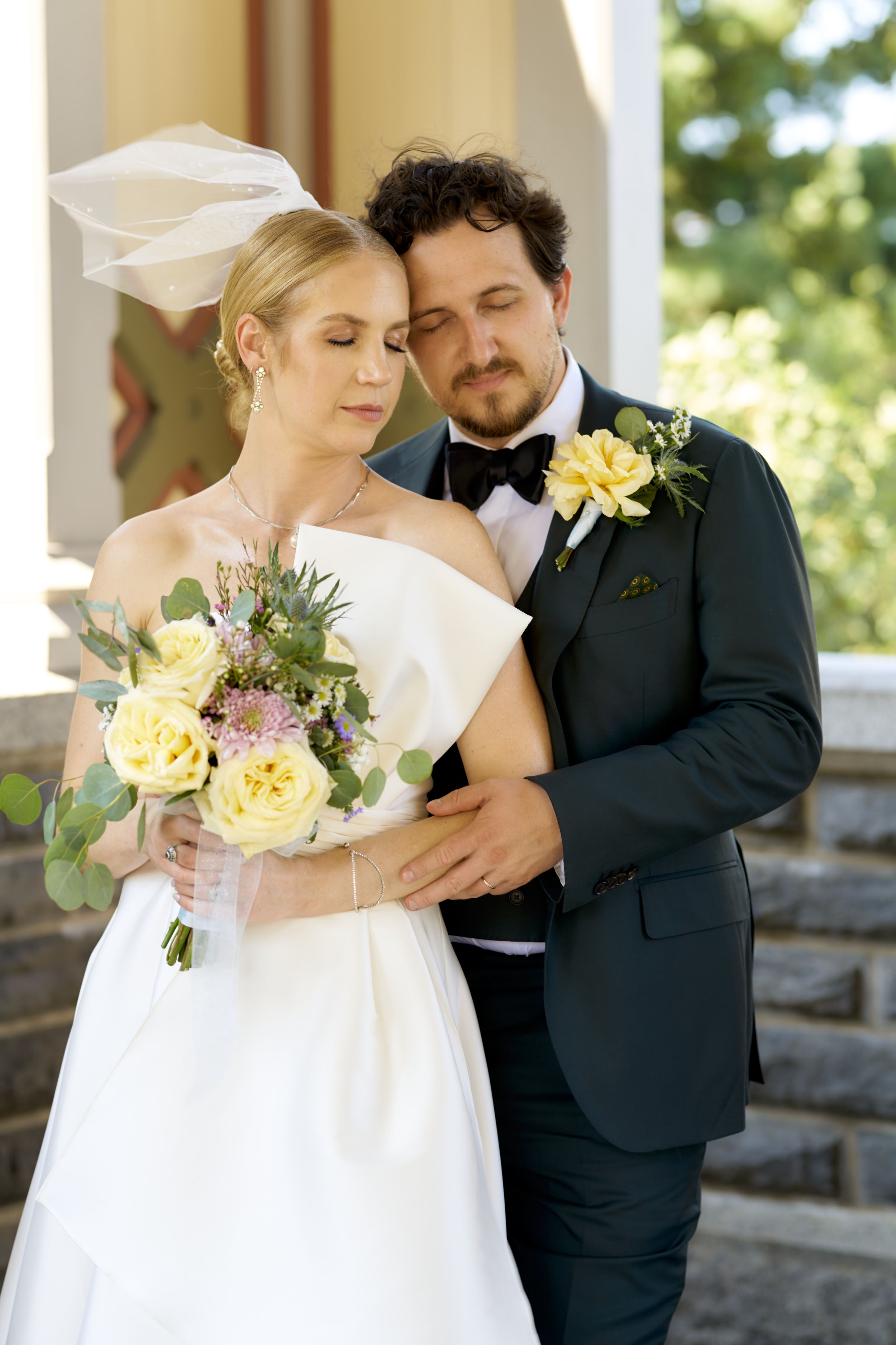 Tender wedding moment with bride holding yellow bouquet as couple poses on stone steps.